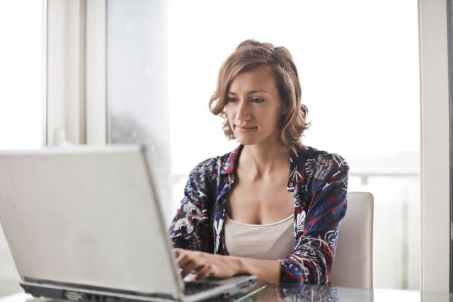 Assistante administrative à distance travaillant sur son ordinateur portable depuis un bureau lumineux