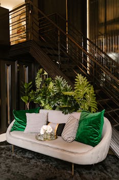 Chic living room featuring a gray couch with green accents under a sleek staircase.