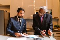 Man in Black Suit Jacket Writing on White Paper