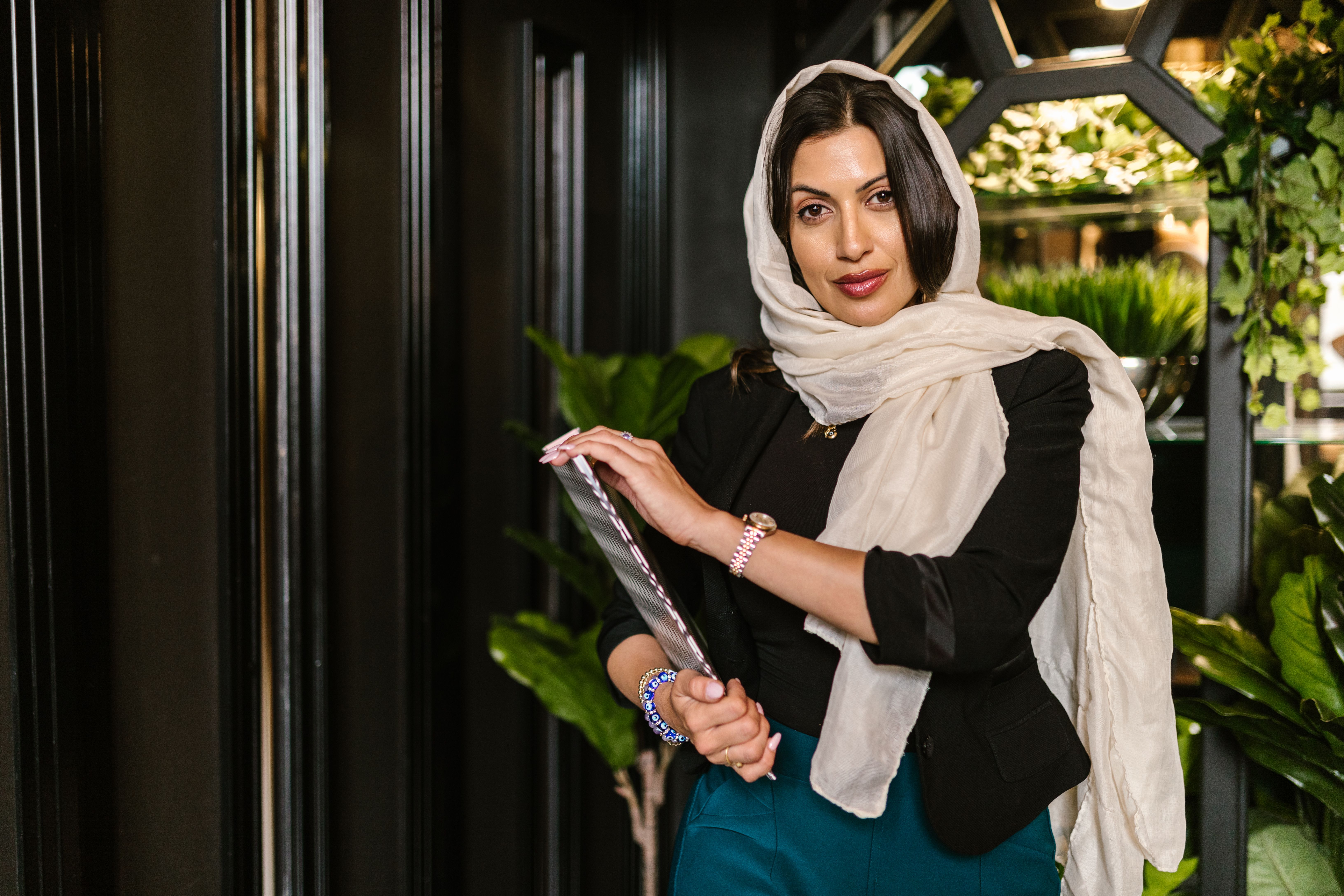 A poised woman in a hijab posing elegantly indoors, showcasing fashion and confidence.