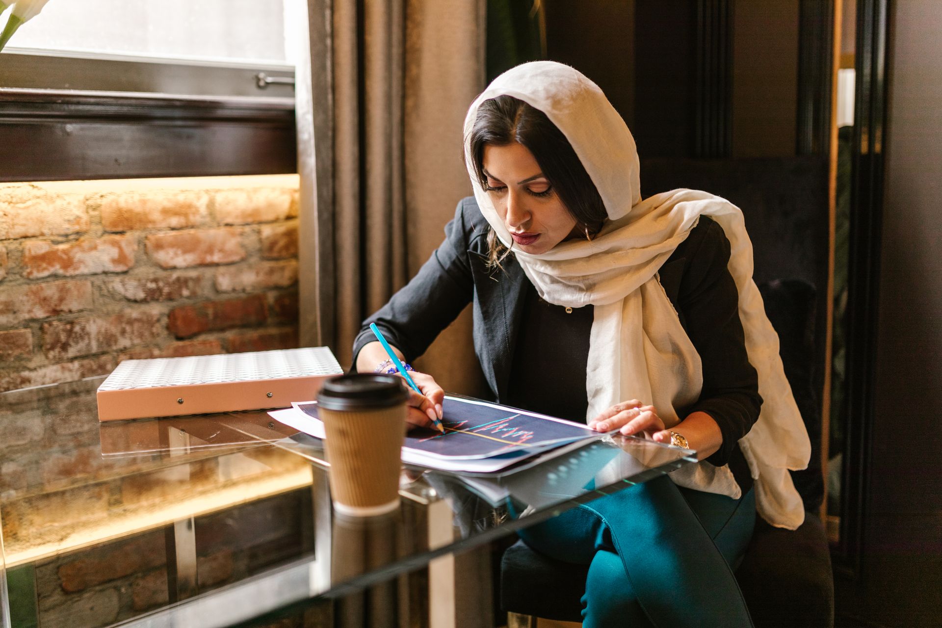Businesswoman in smart attire reviews data charts at a café.