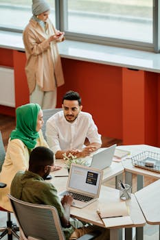 Diverse group of professionals in a modern office discussing projects with laptops.