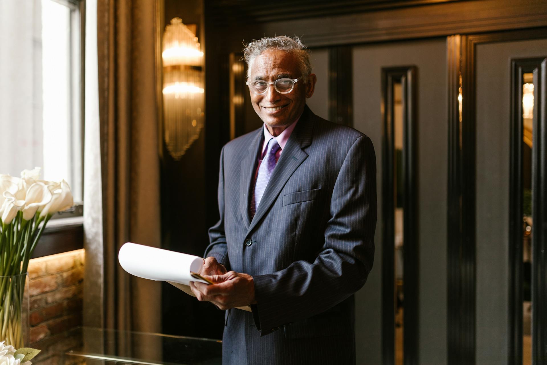 Smiling middle-aged businessman in suit holding document indoors.