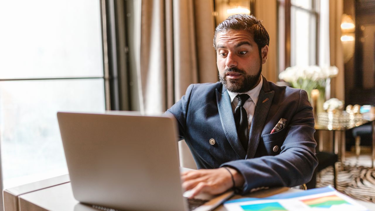 A businessman shows a surprised expression while working on a laptop indoors.