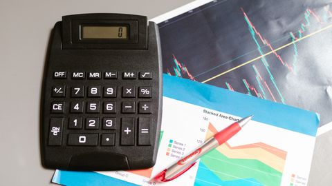Calculator and pen on a desk with financial charts, showcasing analysis and business planning.