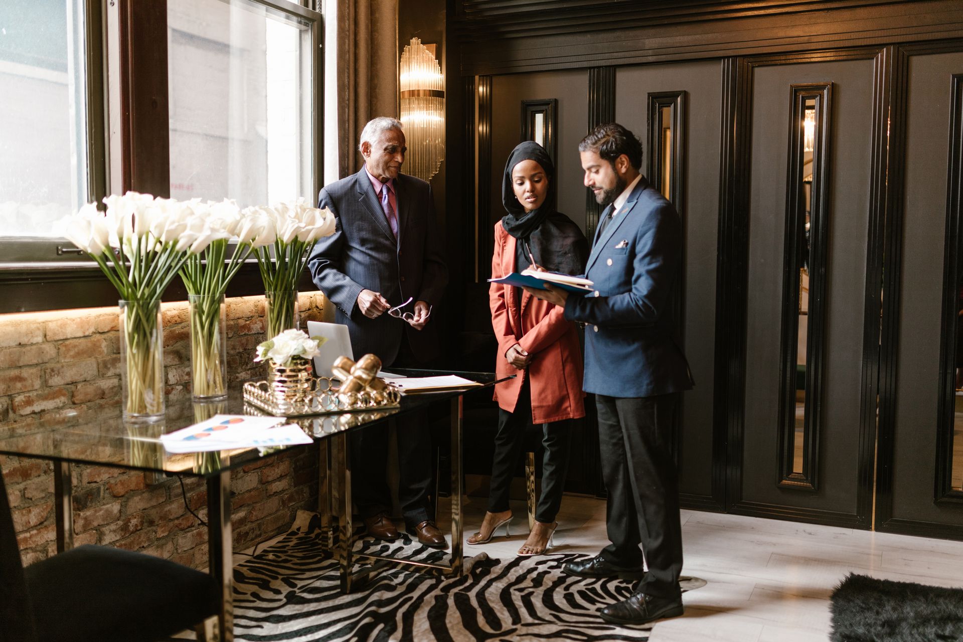 Three professionals in a hotel lobby reviewing documents at a table with white flowers and a zebra-print rug
