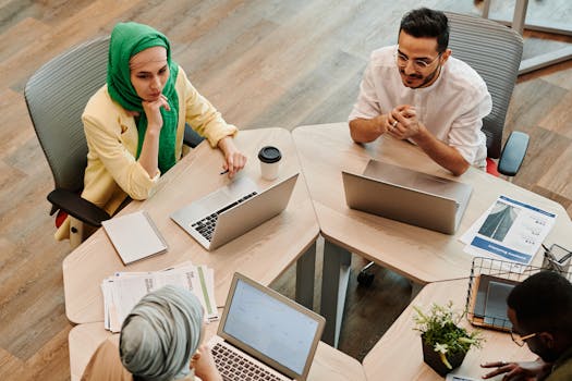 Top view of a diverse team engaged in a discussion with laptops in a modern office environment.