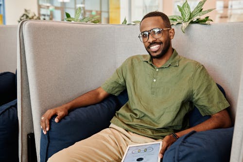 Free A Man Sitting on the Chair Smiling while Wearing Eyeglasses Stock Photo