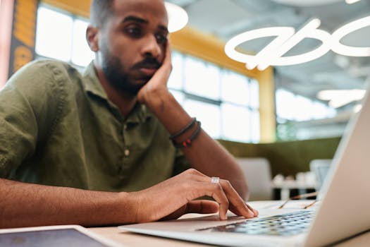 Young man engrossed in work on laptop indoors, showcasing concentration and modern office environment.