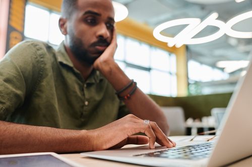 Free Young man engrossed in work on laptop indoors, showcasing concentration and modern office environment. Stock Photo