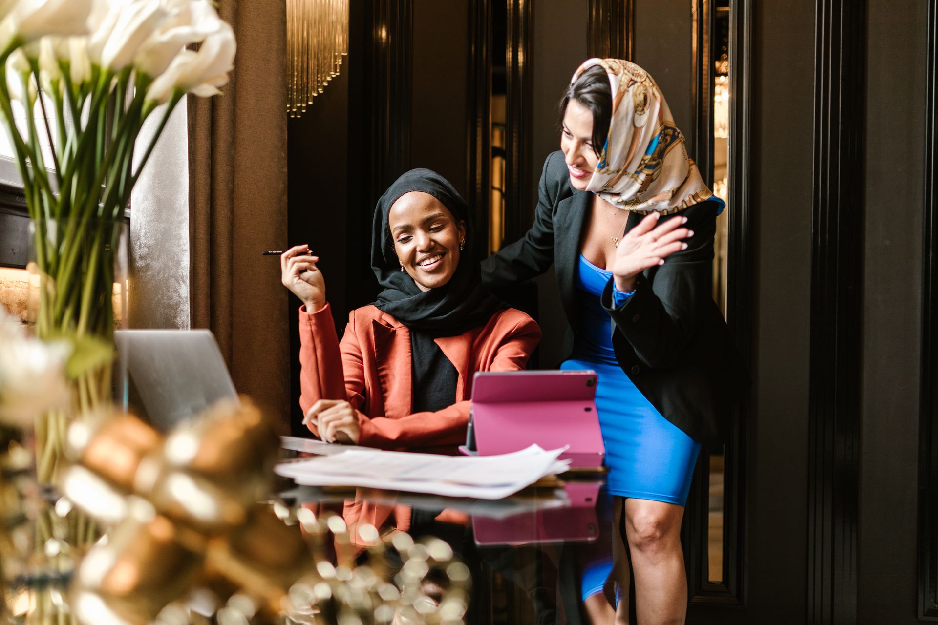 Two businesswomen in hijabs sharing a joyful collaboration moment in an office setting.