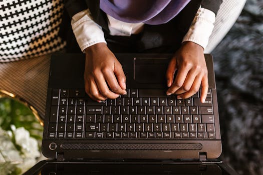 Overhead view of woman's hands typing on a laptop keyboard, symbolizing remote work and technology.