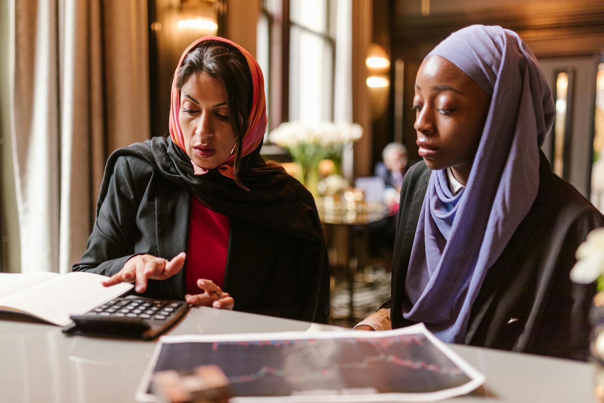 Two multicultural women collaborating on financial analysis using a calculator.