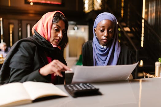 Two women in hijabs engage in a business meeting, analyzing documents in an office setting.