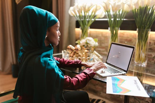 A woman in a hijab typing on a laptop at an office desk.