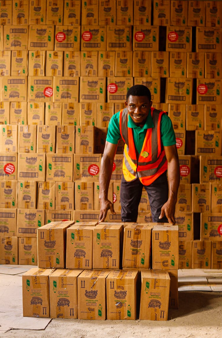 Man Working In A Warehouse Standing Between Piles Of Boxes