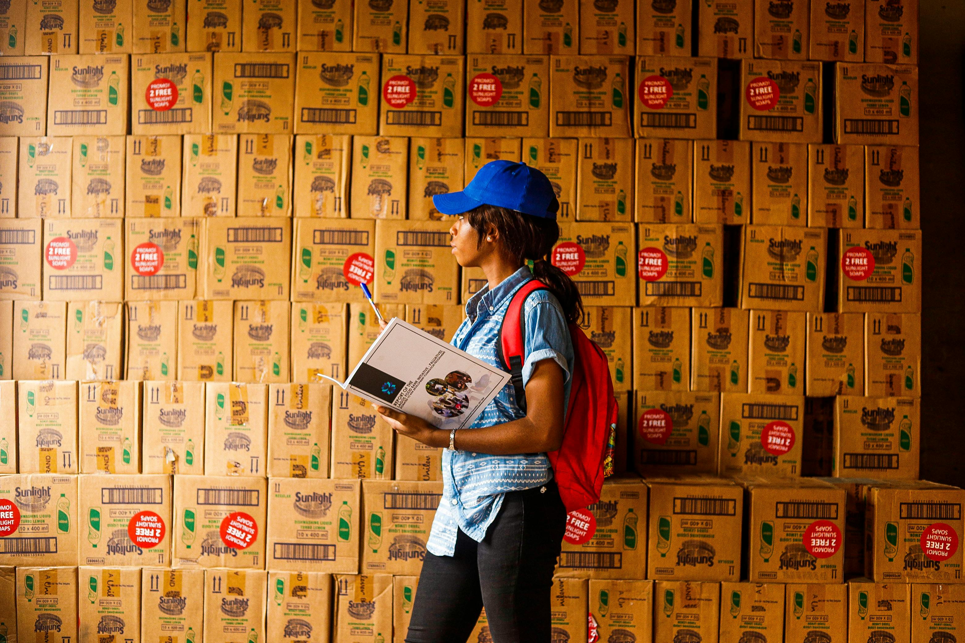 Woman in warehouse checking inventory with boxes around her, emphasizing logistics.