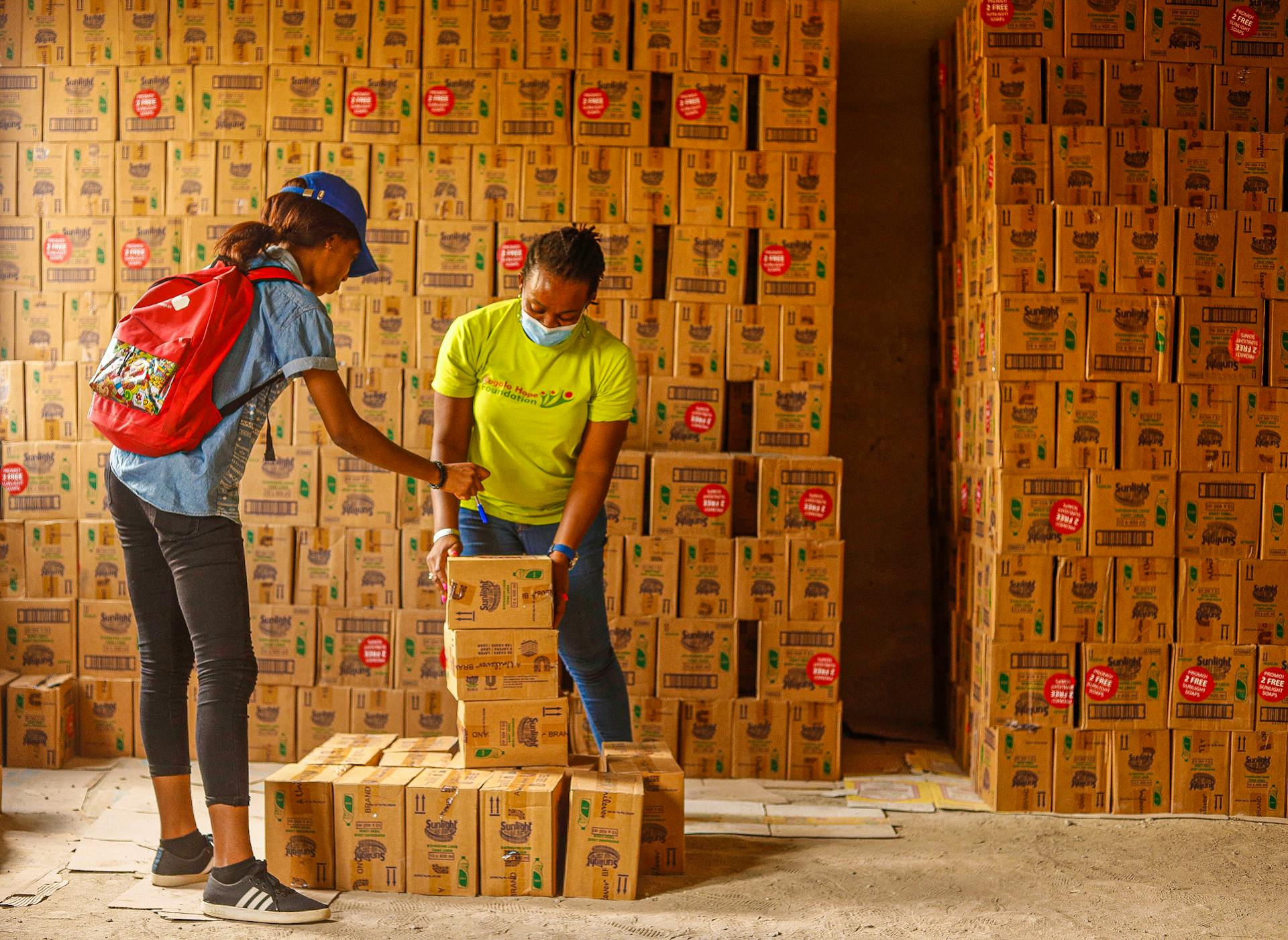 Two women managing inventory in a box-filled warehouse, ensuring organization and safety.