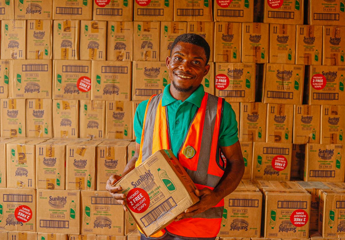 Warehouse employee holding a box while smiling in a stockroom filled with Sunlight boxes.