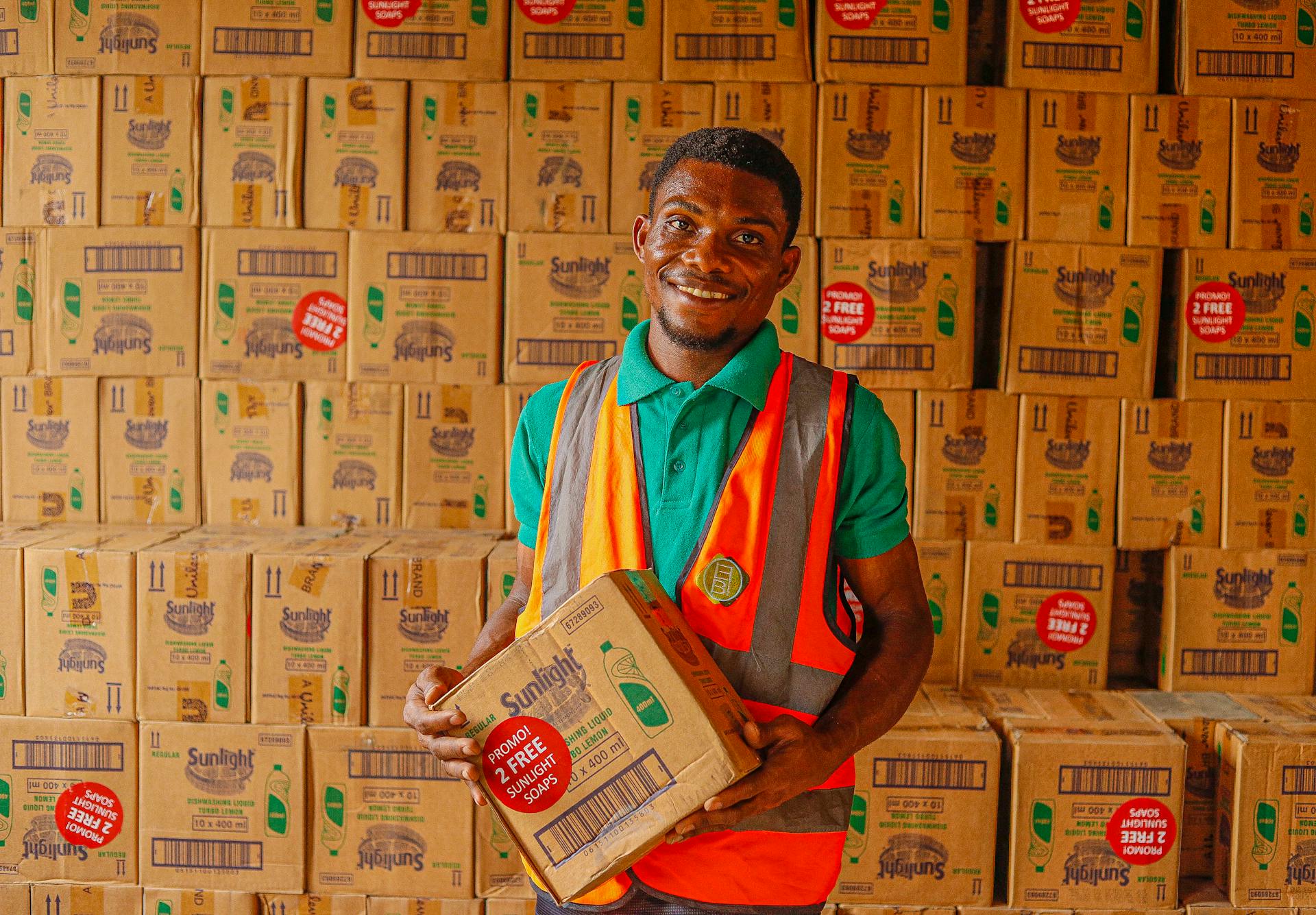 Warehouse employee holding a box while smiling in a stockroom filled with Sunlight boxes.