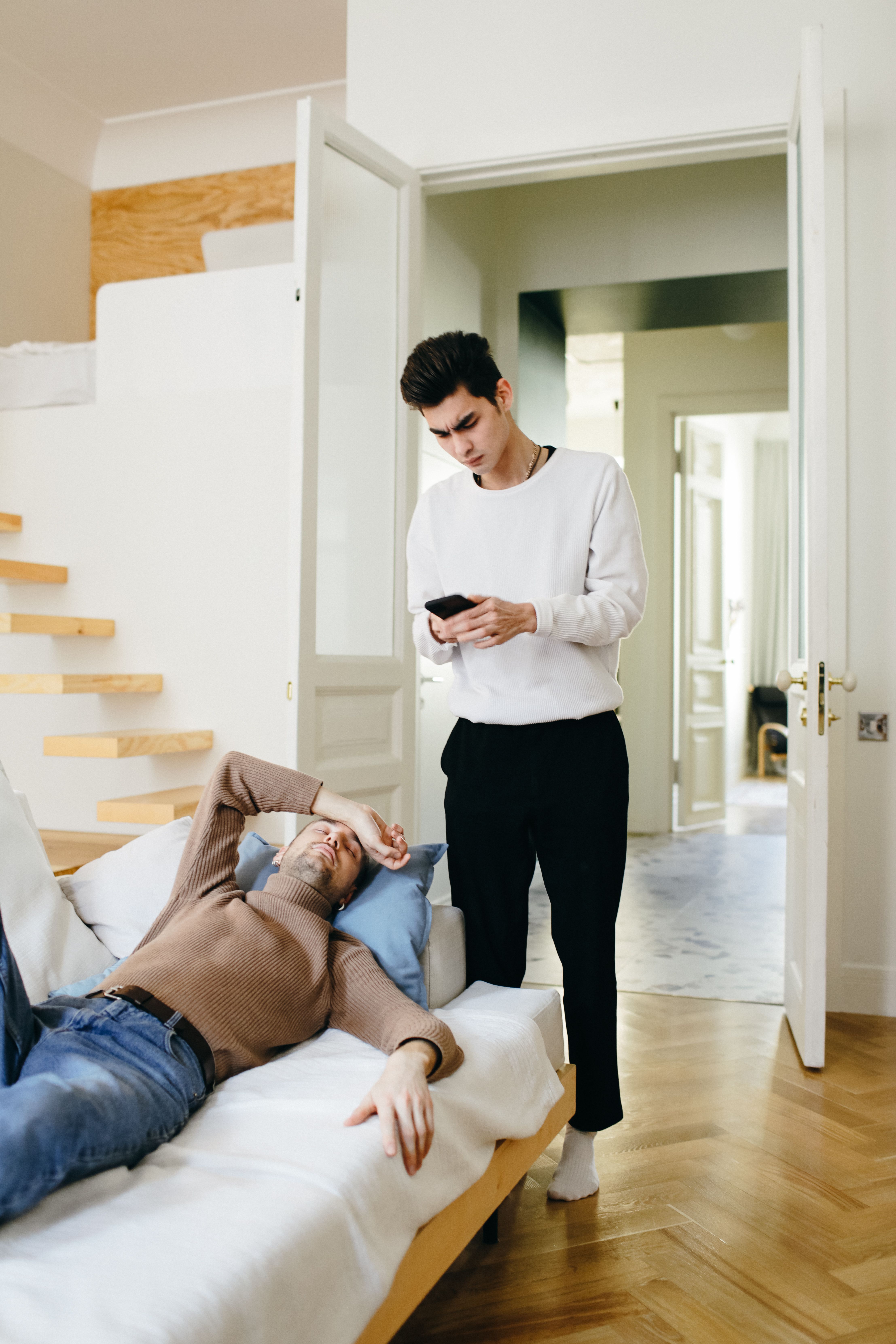 A peaceful moment between an interracial couple in a modern bedroom setting, one using a smartphone.