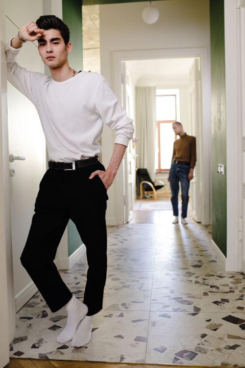 Free A young man in a white sweater stands stylishly in a modern hallway, showcasing casual home fashion. Stock Photo