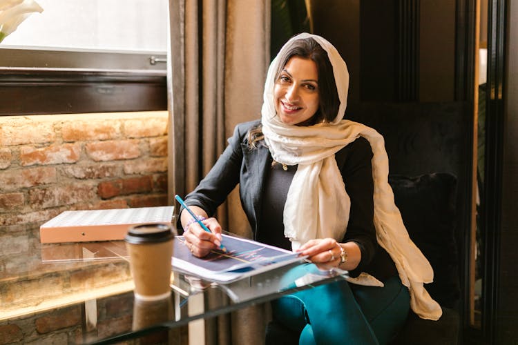 Smiling Woman With Hijab Sitting At Glass Desk In Office