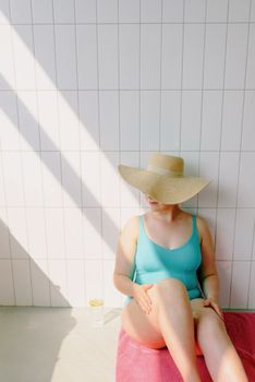 A woman in a teal swimsuit and straw hat enjoys a sunny day by the pool area.
