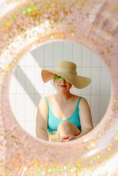 Woman in swimwear and sun hat seen through inflatable pool float. Bright summer vibes.