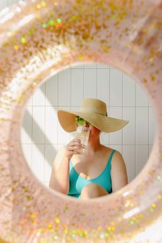 Woman in a straw hat drinking water through a ring float on a sunny summer day.