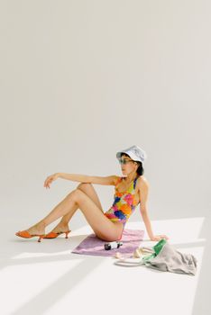 A woman in colorful swimwear and bucket hat poses on a towel, embodying summer style.