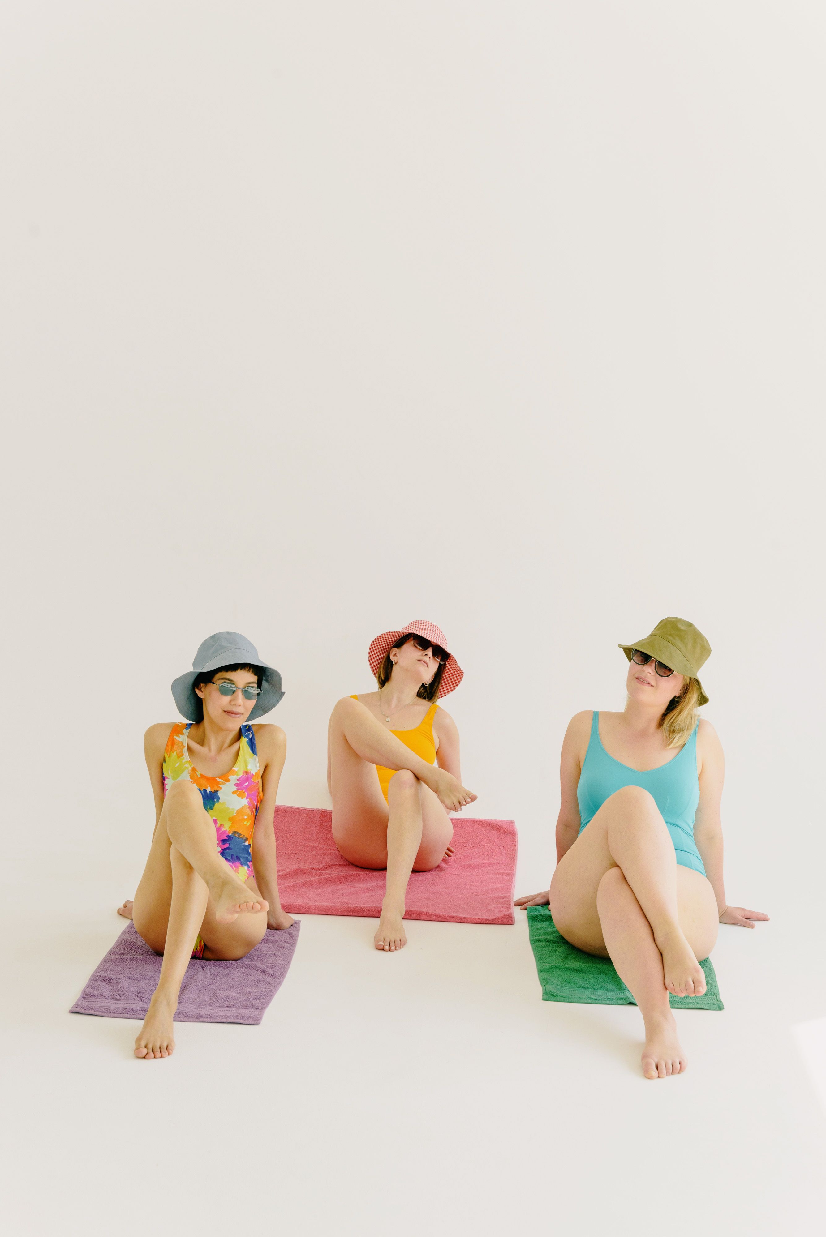 Three women in colorful swimsuits and hats sitting indoors on mats.