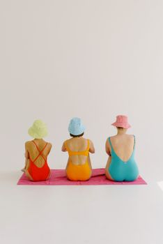 Three women in vibrant swimsuits and bucket hats sitting indoors for a studio shoot.