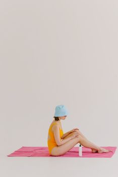 Woman in a swimsuit sitting on a towel indoors, highlighting sun protection.