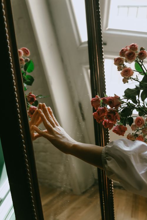 Free A hand gently touches a mirror with pink roses reflected, creating a serene atmosphere. Stock Photo