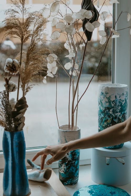 Free A hand arranges dried flowers in artistic vases by a window. Stock Photo