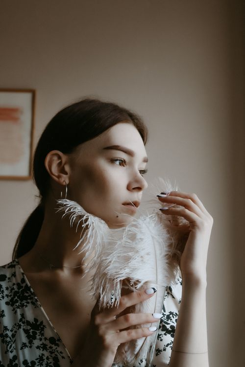 Free A contemplative woman holding a feather by natural light, creating a serene atmosphere. Stock Photo