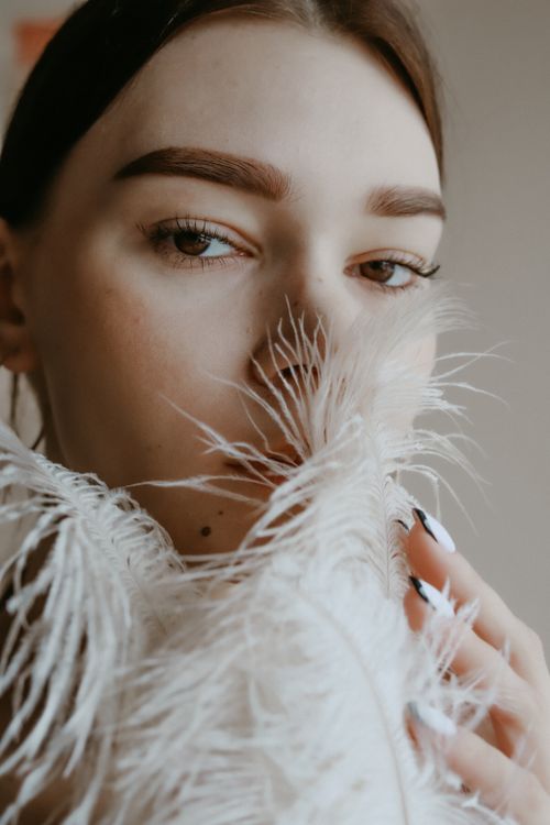 Free Close-up portrait of a woman with brown hair, holding white feathers with a mysterious expression. Stock Photo