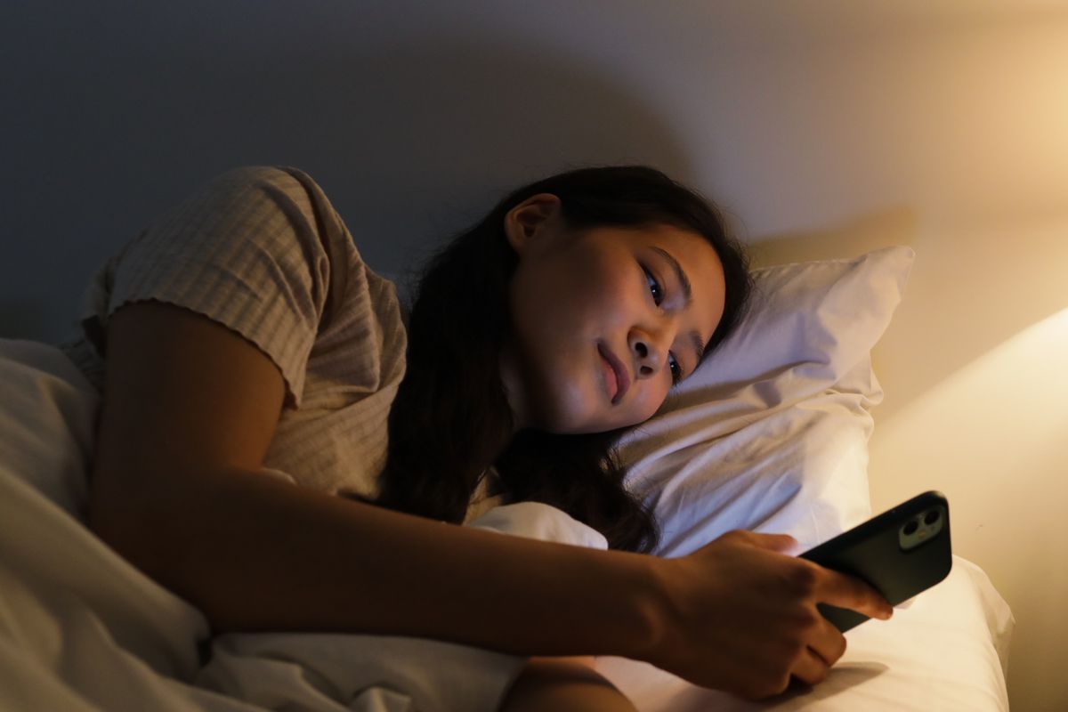 Woman lying on a bed using her smartphone late at night illustrating screen time habit.