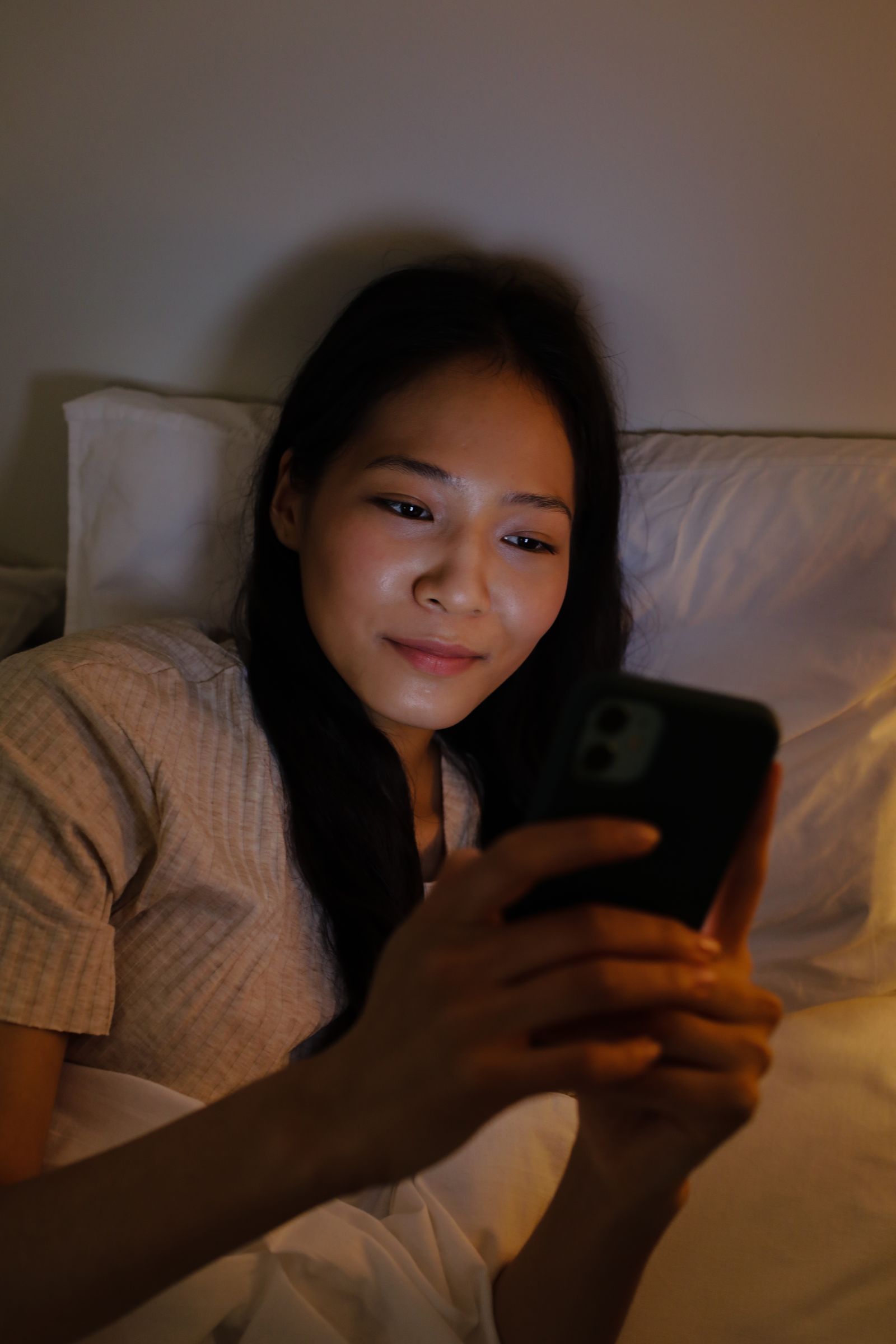 Young Asian woman using her smartphone while relaxing in bed