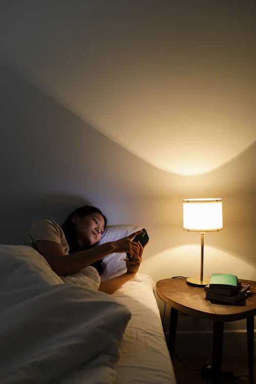 Free A Woman Using Her Smartphone While on the Bed  Stock Photo