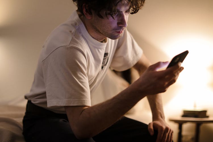 
A Man In A White Shirt Using His Smartphone 