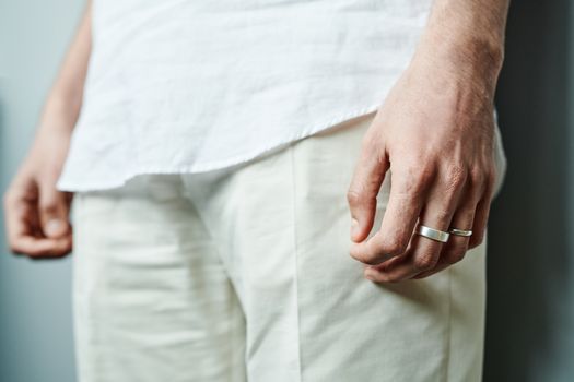 A detailed close-up of a person's hand wearing silver rings, dressed in white clothing.