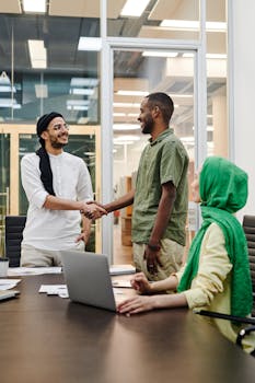 Three professionals engage in a meeting, showcasing diversity and teamwork through a handshake.
