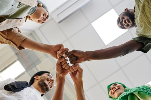 Free A diverse group of colleagues perform a fist bump in an office setting, symbolizing teamwork. Stock Photo