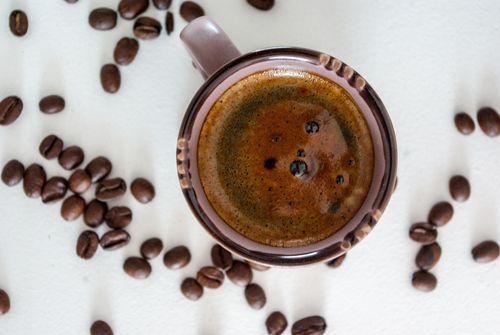 Free Top view of coffee mug with frothy espresso and scattered coffee beans on white background. Stock Photo