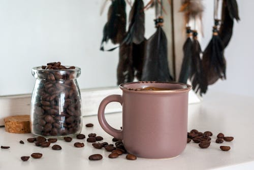 
A Close-Up Shot of a Cup of Coffee beside a Glass Container with Coffee Beans