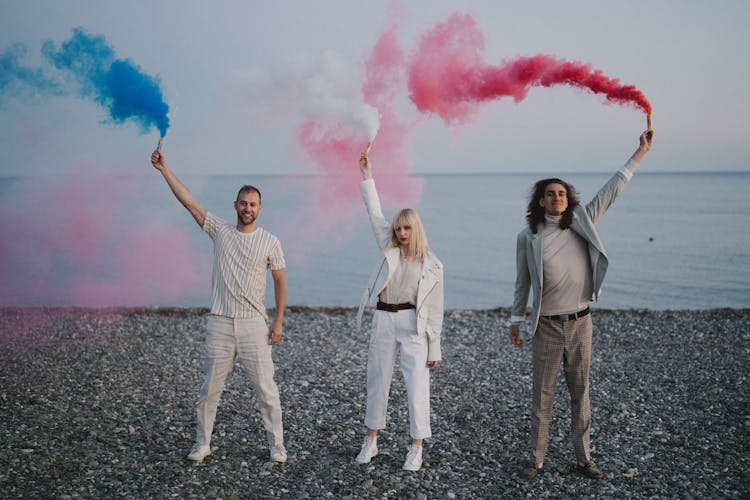 
People Holding Smoke Bombs On A Shore