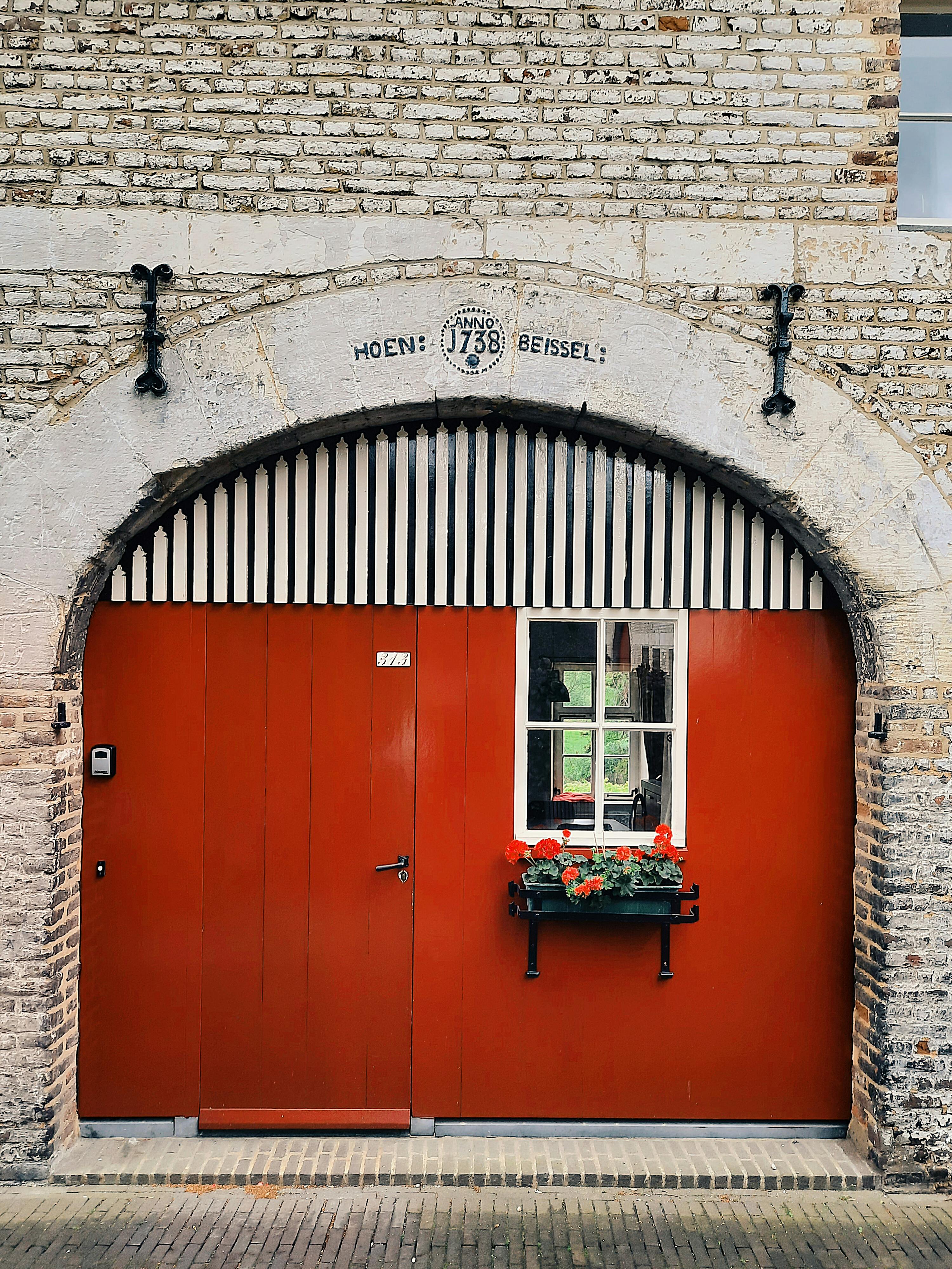 Charming red door with floral decoration at a historic brick building.