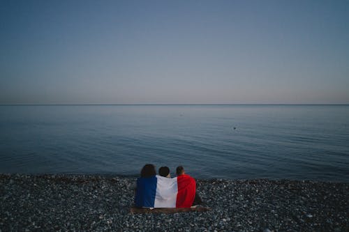 Friends Sitting on a Rocky Shore with the Flag of France on Their Back